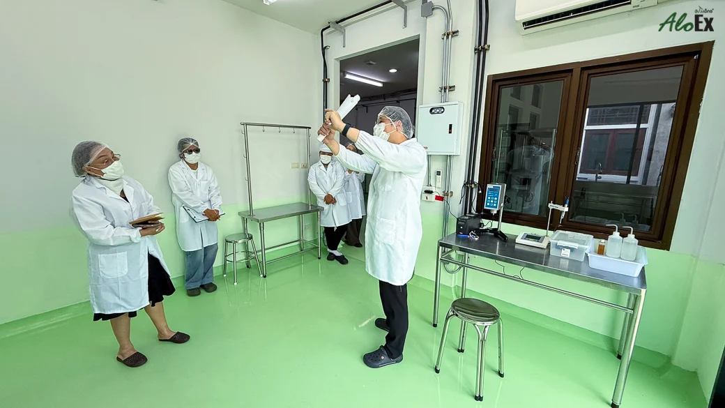 An auditor and the team lifting a sample container for inspection in the AloEx production area