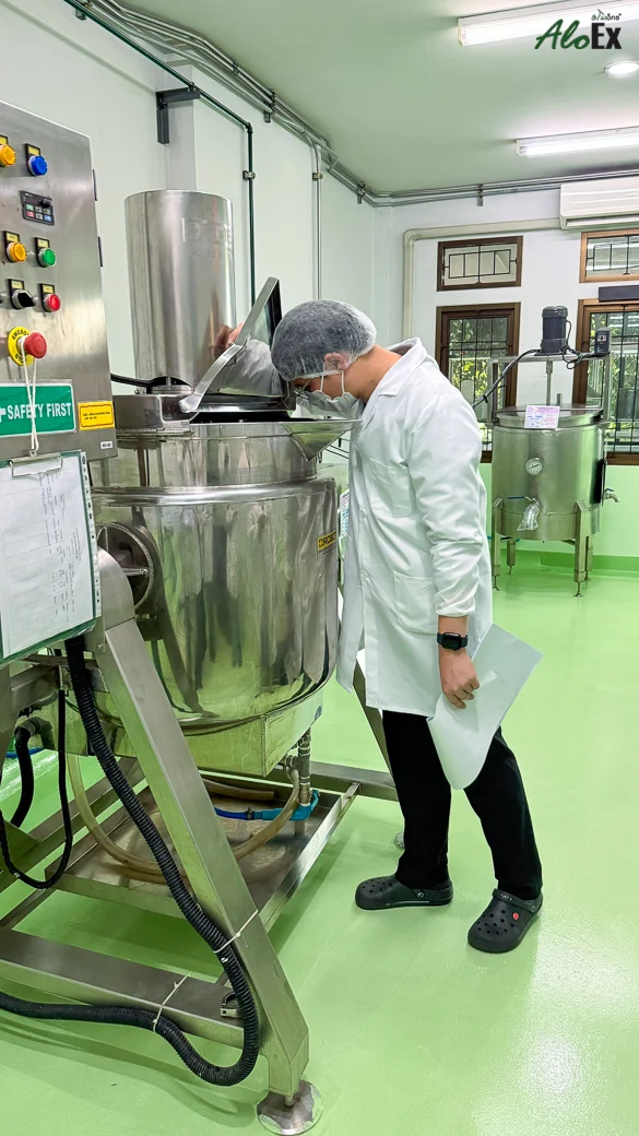 A member of staff in a gown and hair net checking a mixing tank in the AloEx production room