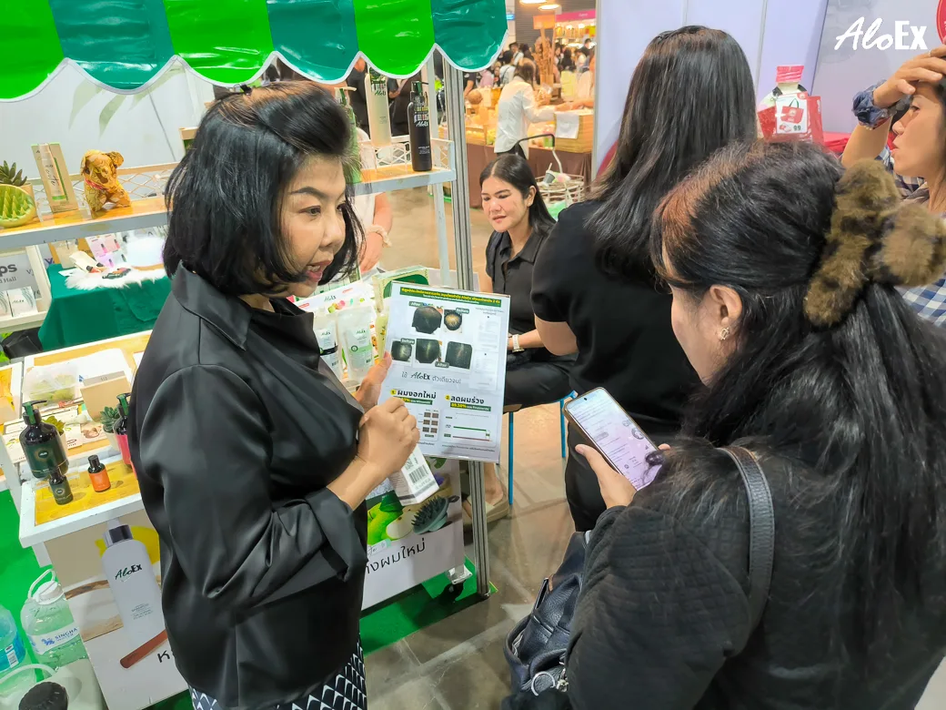 พนักงาน AloEx อธิบายผลลัพธ์ก่อน-หลังการใช้ผลิตภัณฑ์ให้ผู้เข้าชมฟังที่บูธ B20