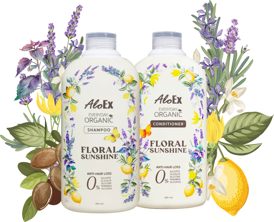 Chai dầu gội và dầu xả AloEx Everyday Organic Floral Sunshine đặt cạnh nhau, bao quanh là hoa oải hương, hoàng lan, chanh và hạt argan